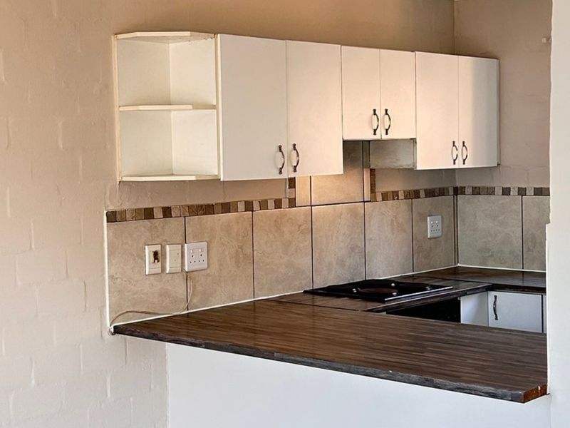 A compact kitchen area featuring white cabinetry, a dark laminate countertop, and a tiled backsplash with an integrated electric hob.