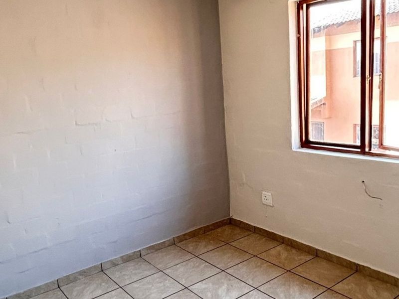 An empty bedroom featuring tiled flooring and a timber window frame, requiring minor cosmetic repairs to the wall plaster and electrical fixtures.