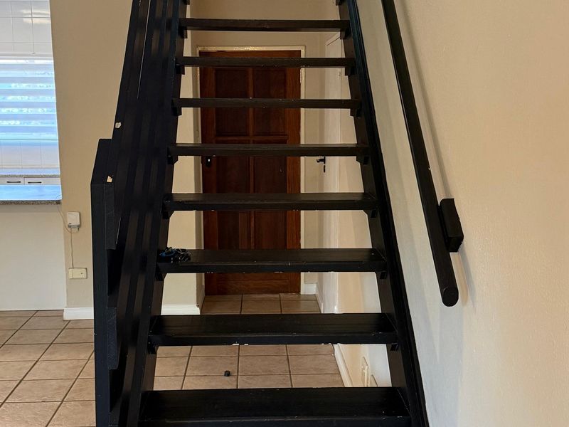 A central hallway featuring a dark painted staircase with a handrail, leading towards a timber door, with tiled flooring throughout.