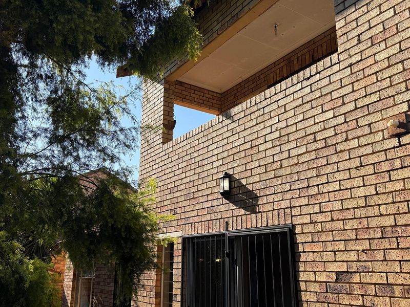 Rear view of the townhouse featuring a face brick facade, a balcony with an unfinished ceiling, and a secure entrance gate.