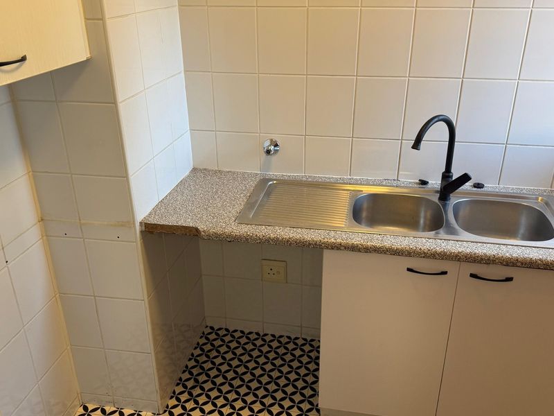 A functional laundry area featuring a double stainless steel sink, black faucet, tiled splashback, and built-in cabinetry with a laminate countertop.