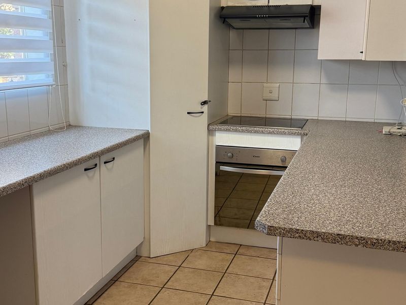 A functional kitchen featuring laminate countertops, built-in oven, electric hob, extractor fan, and tiled flooring with neutral cabinetry.
