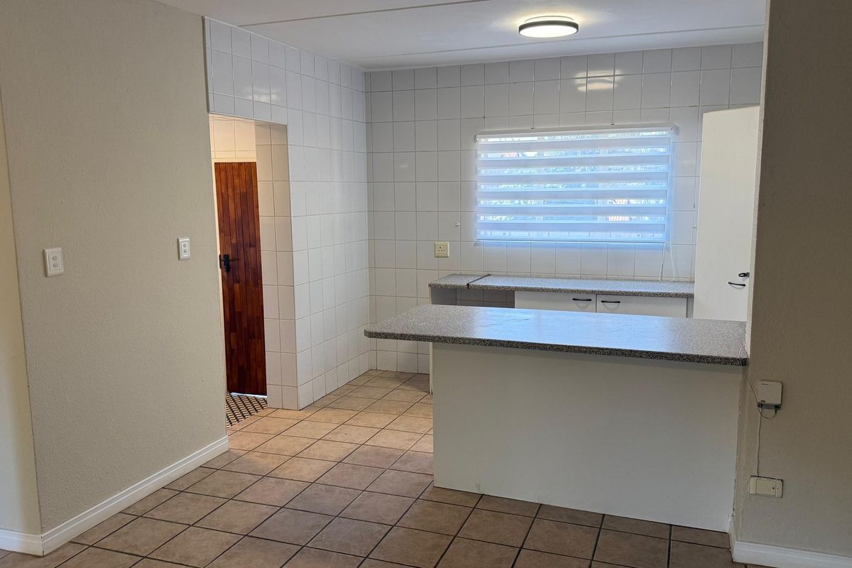 A functional, empty kitchen area featuring tiled walls, tiled flooring, and a breakfast bar with laminate countertops, ready for personalization.