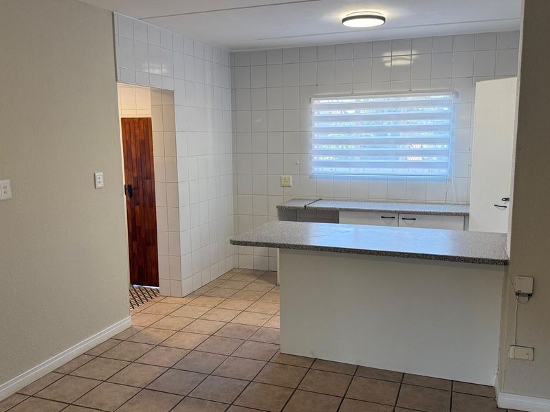 A functional, empty kitchen area featuring tiled walls, tiled flooring, and a breakfast bar with laminate countertops, ready for personalization.