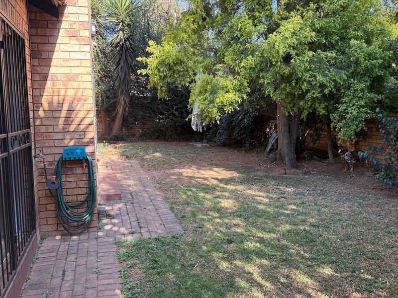A private rear garden featuring brick paving, established trees, and a brick boundary wall, offering potential for landscaping and outdoor living improvements.