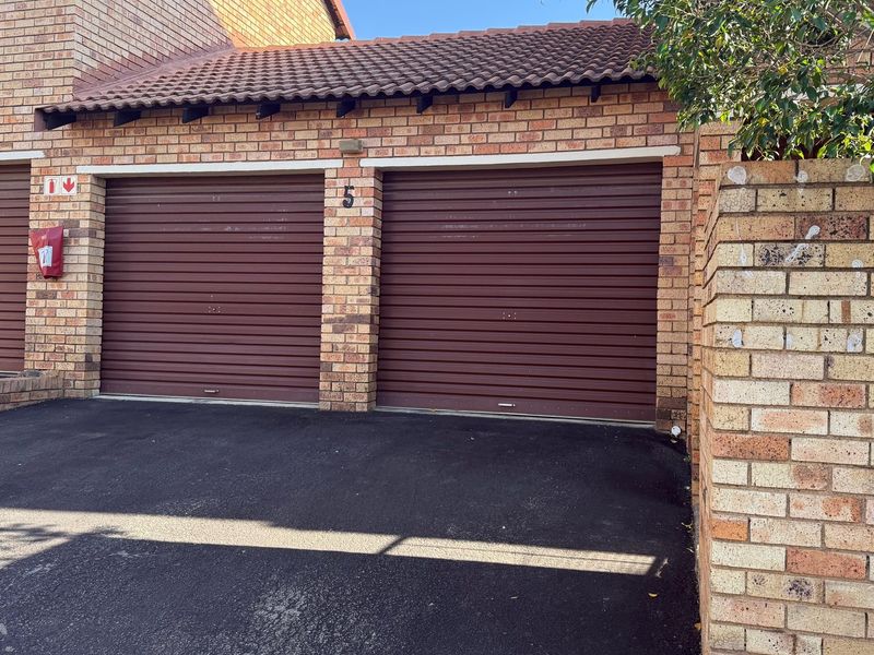 Exterior view of a townhouse garage block featuring two roll-up garage doors, brick construction, and a paved driveway area.