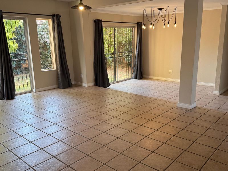 Spacious open-plan living and dining area featuring neutral ceramic floor tiles, structural columns, and sliding glass doors providing access to the garden.