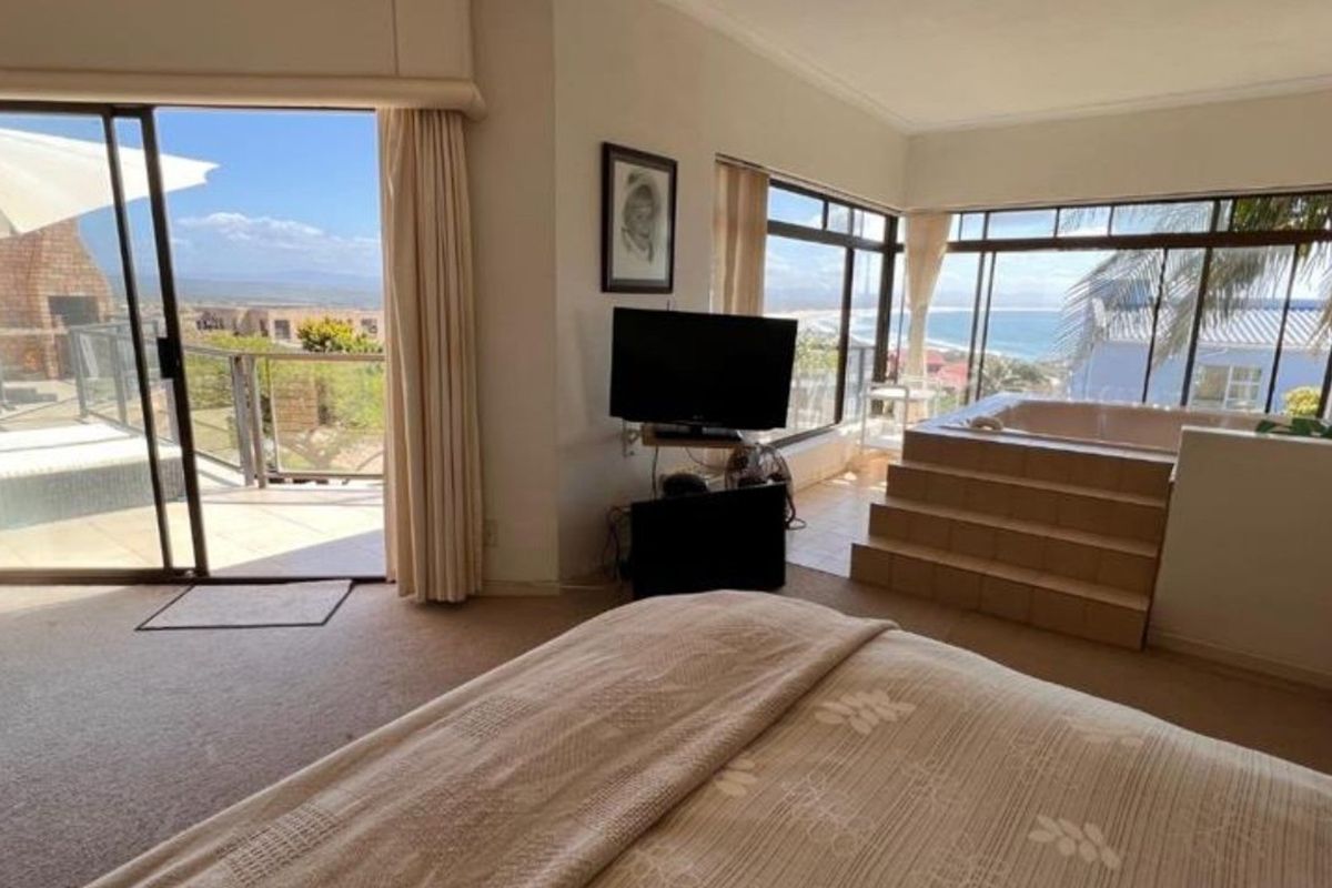 Spacious bedroom featuring a built-in bathtub, large windows with ocean views, and sliding glass doors leading to an outdoor balcony area.