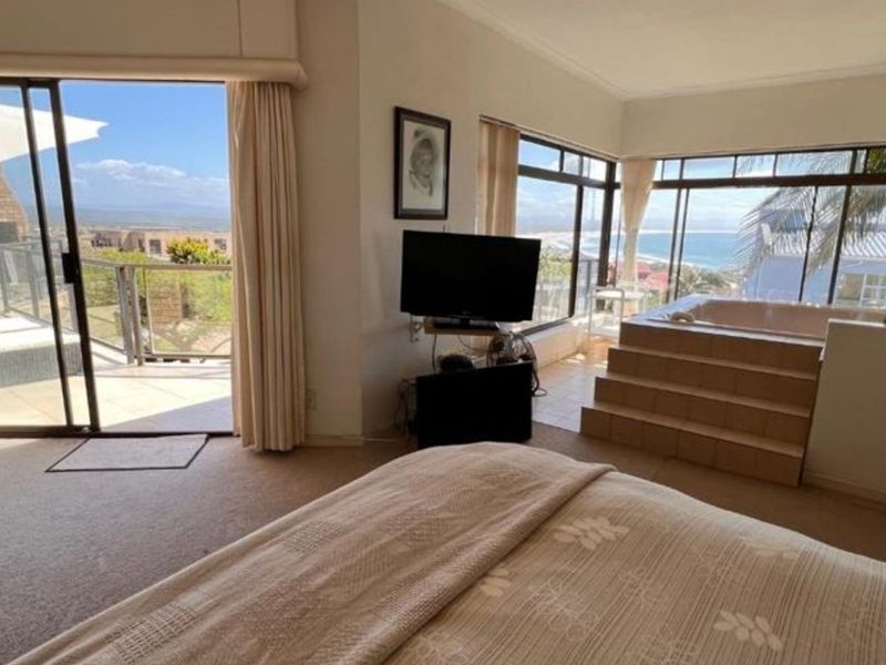 Spacious bedroom featuring a built-in bathtub, large windows with ocean views, and sliding glass doors leading to an outdoor balcony area.