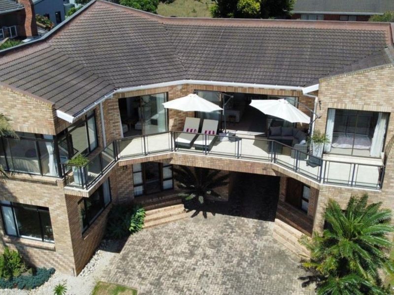 Aerial view of a multi-level brick residence featuring a spacious balcony, paved driveway, and modern architectural design.
