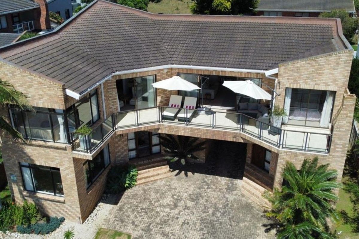 Aerial view of a multi-level brick residence featuring a spacious balcony, paved driveway, and modern architectural design.
