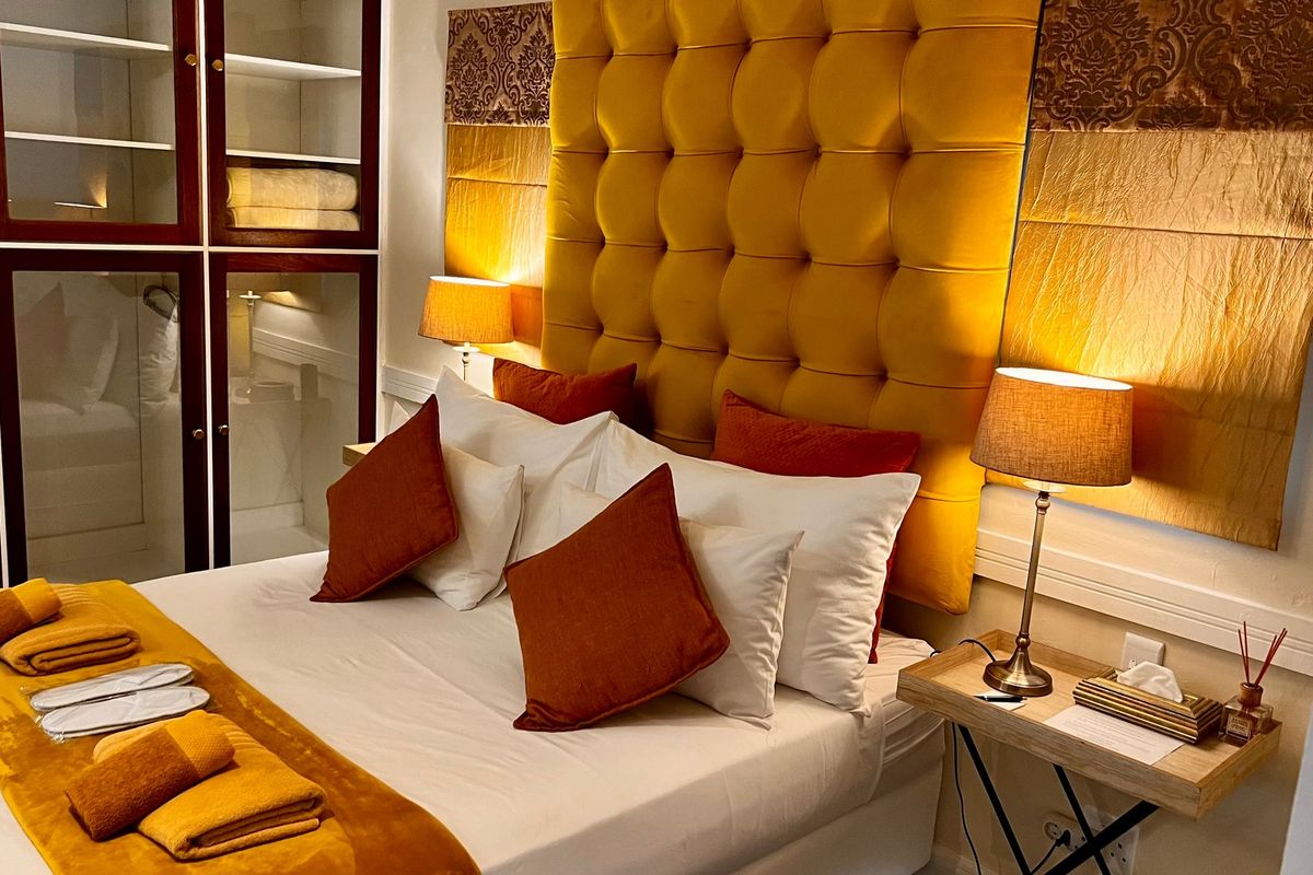 A well-appointed bedroom featuring a large tufted yellow headboard and integrated glass-fronted cabinetry for storage.