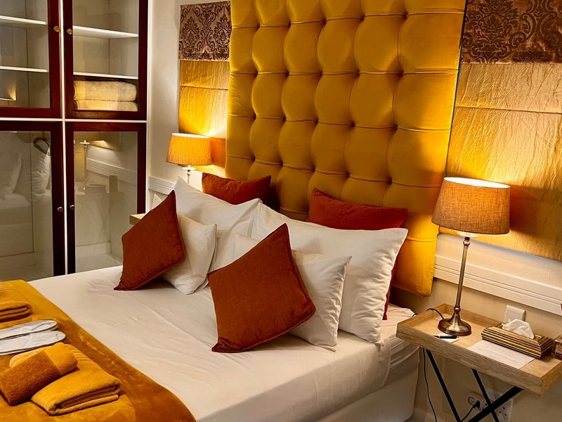 A well-appointed bedroom featuring a large tufted yellow headboard and integrated glass-fronted cabinetry for storage.