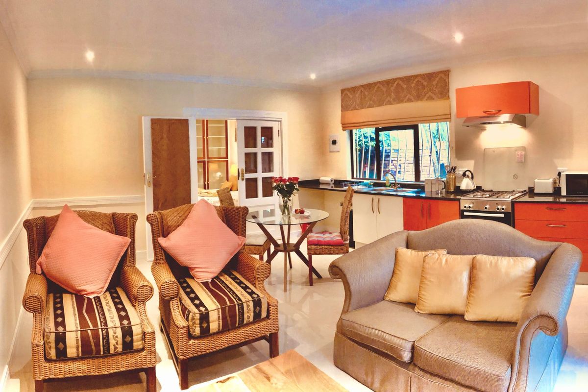 Open-plan living area featuring a functional kitchen with orange cabinetry, gas hob, and tiled flooring, seamlessly connected to a comfortable lounge space.