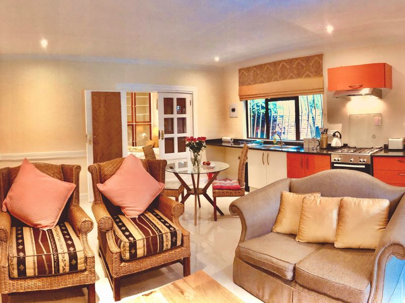 Open-plan living area featuring a functional kitchen with orange cabinetry, gas hob, and tiled flooring, seamlessly connected to a comfortable lounge space.