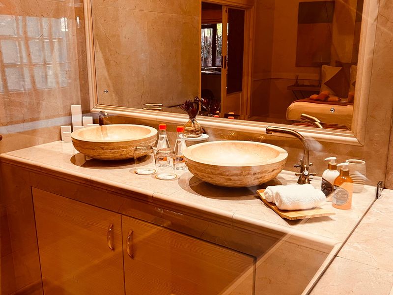 A well-appointed bathroom featuring a marble vanity with double stone vessel sinks, brass fixtures, and extensive marble wall tiling.
