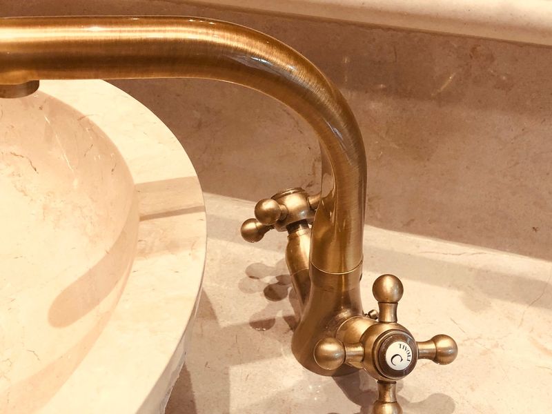 Close-up view of a classic brass faucet set against a polished marble vanity countertop and integrated sink.