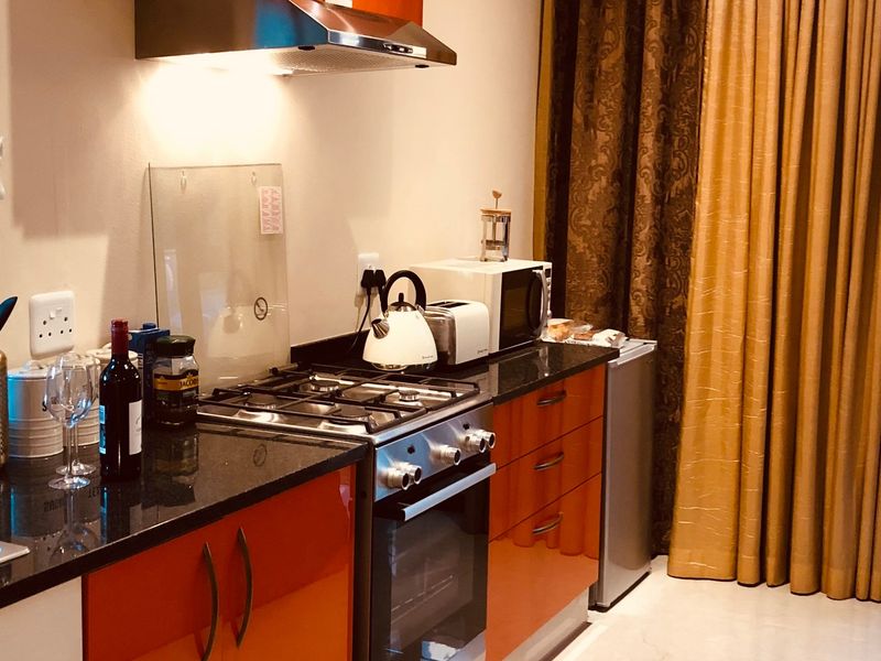 Compact kitchen featuring orange high-gloss cabinetry, granite countertops, a gas stove with extractor fan, and direct access to an outdoor area.
