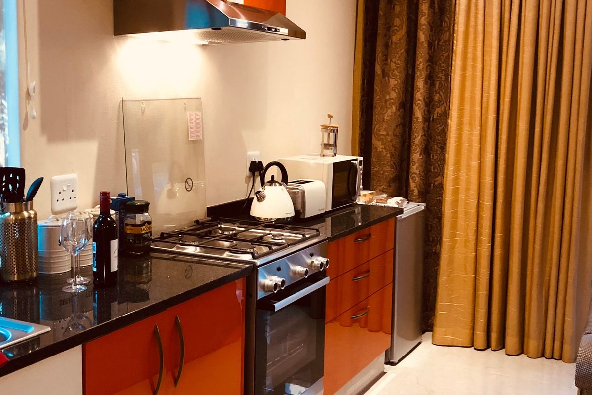 Compact kitchen featuring orange high-gloss cabinetry, granite countertops, a gas stove with extractor fan, and direct access to an outdoor area.