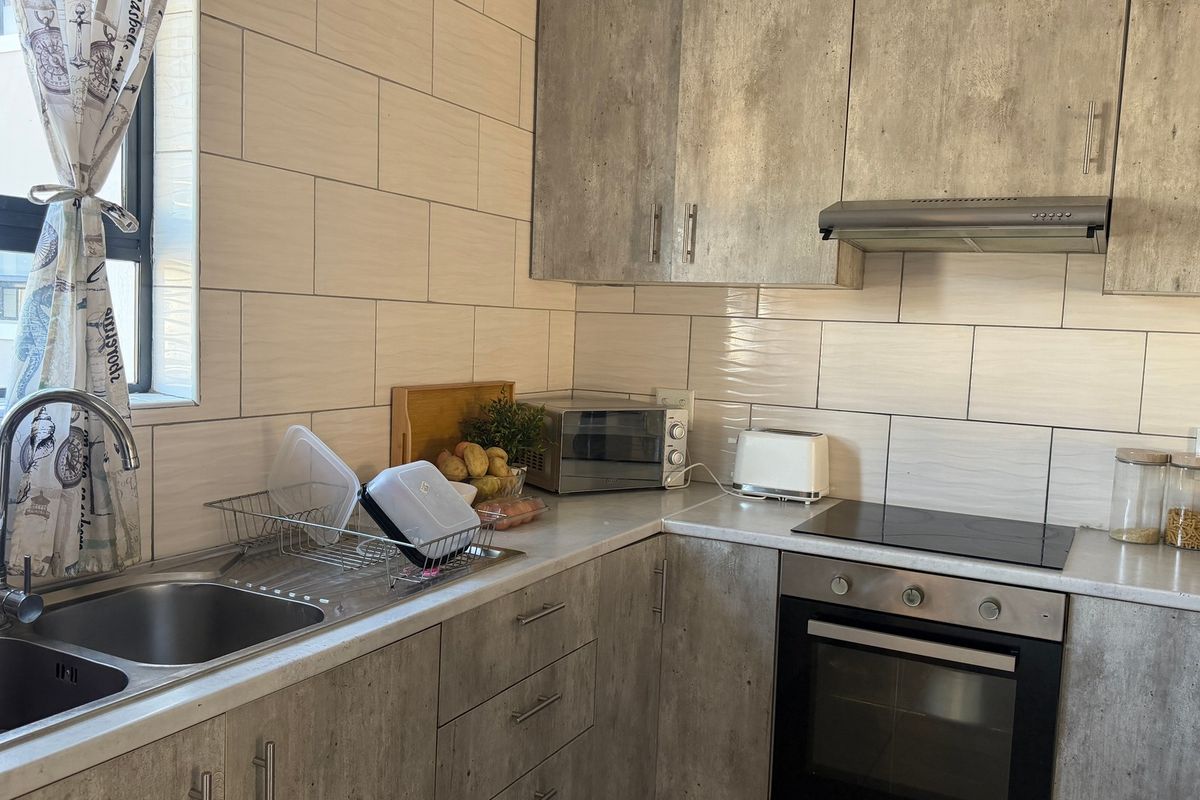 A functional kitchen featuring modern laminate cabinetry, a stainless steel double sink, subway tile backsplash, and integrated cooking appliances.