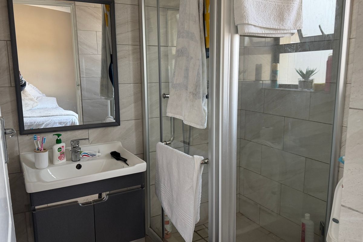 A functional bathroom featuring a modern vanity cabinet, basin, wall mirror, and a glass-enclosed shower with neutral wall tiling.