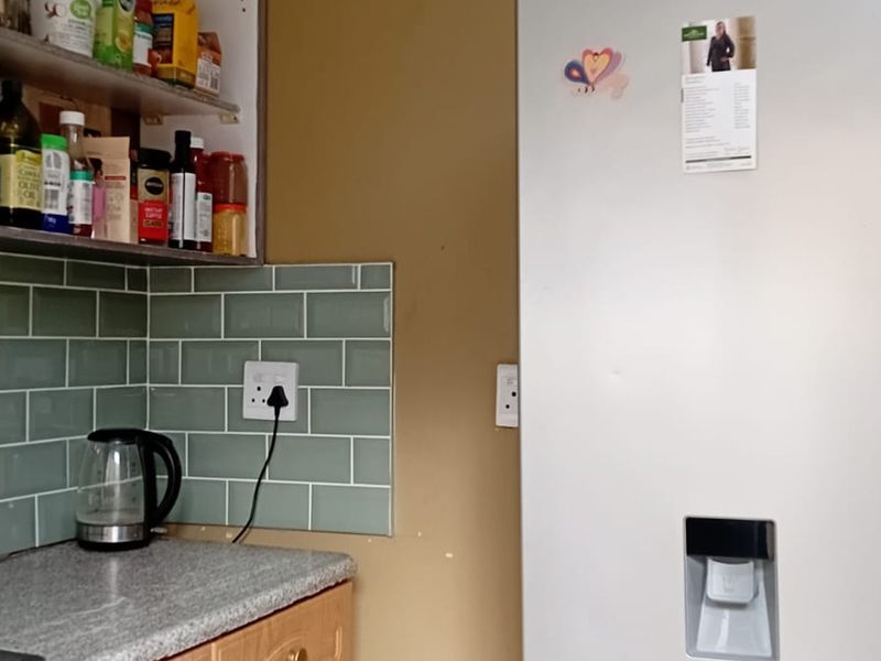 A kitchen corner featuring a green subway tile backsplash, laminate countertops, and built-in cabinetry, showing signs of wear on the surrounding wall surfaces.