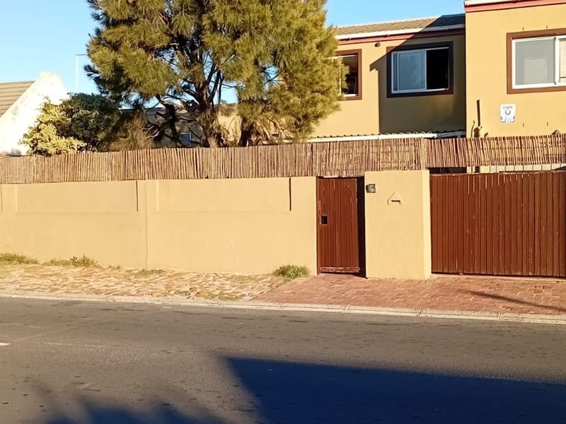 Front exterior view of the townhouse featuring a secure boundary wall, timber gates, and a paved driveway entrance.