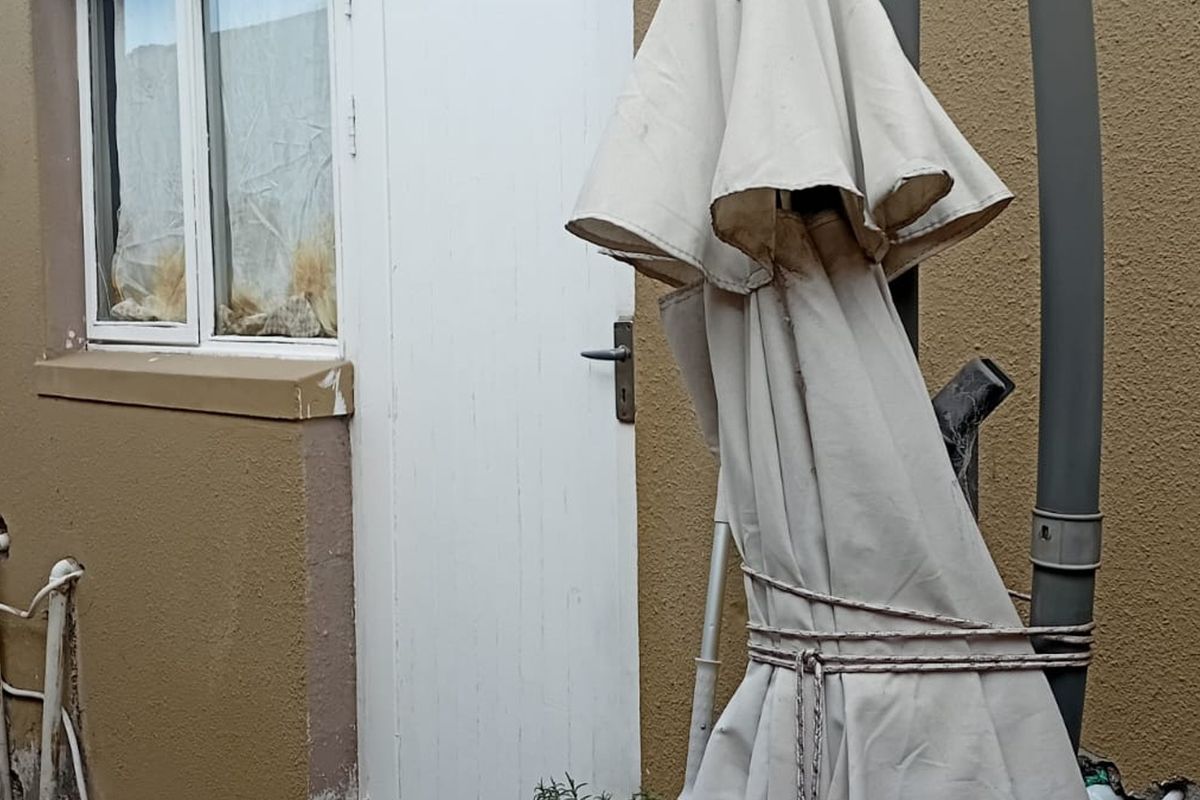 A view of the rear exterior wall showing exposed plumbing, a window, and a door, indicating a need for maintenance and exterior upkeep.