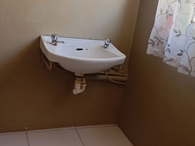 A basic bathroom featuring a wall-mounted basin with exposed plumbing and tiled flooring.