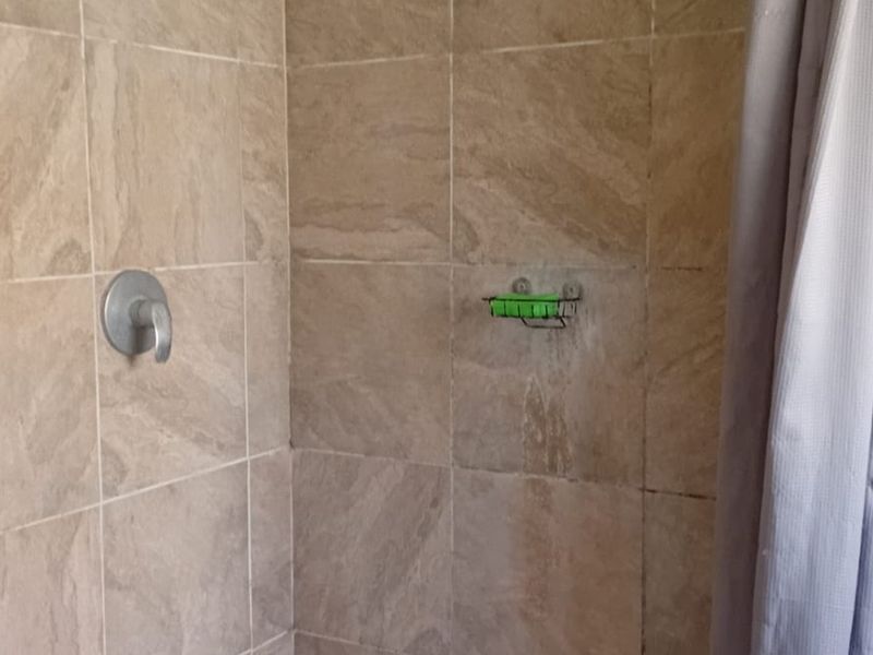 A shower enclosure featuring neutral-toned wall tiles, a standard shower mixer, and a shower curtain, requiring maintenance to address grout and tile surface staining.