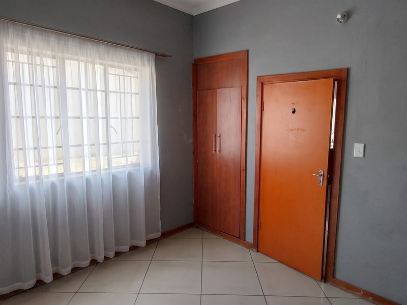 A vacant bedroom featuring tiled flooring, a built-in wardrobe, and a window with security bars, offering a neutral canvas for personalization.