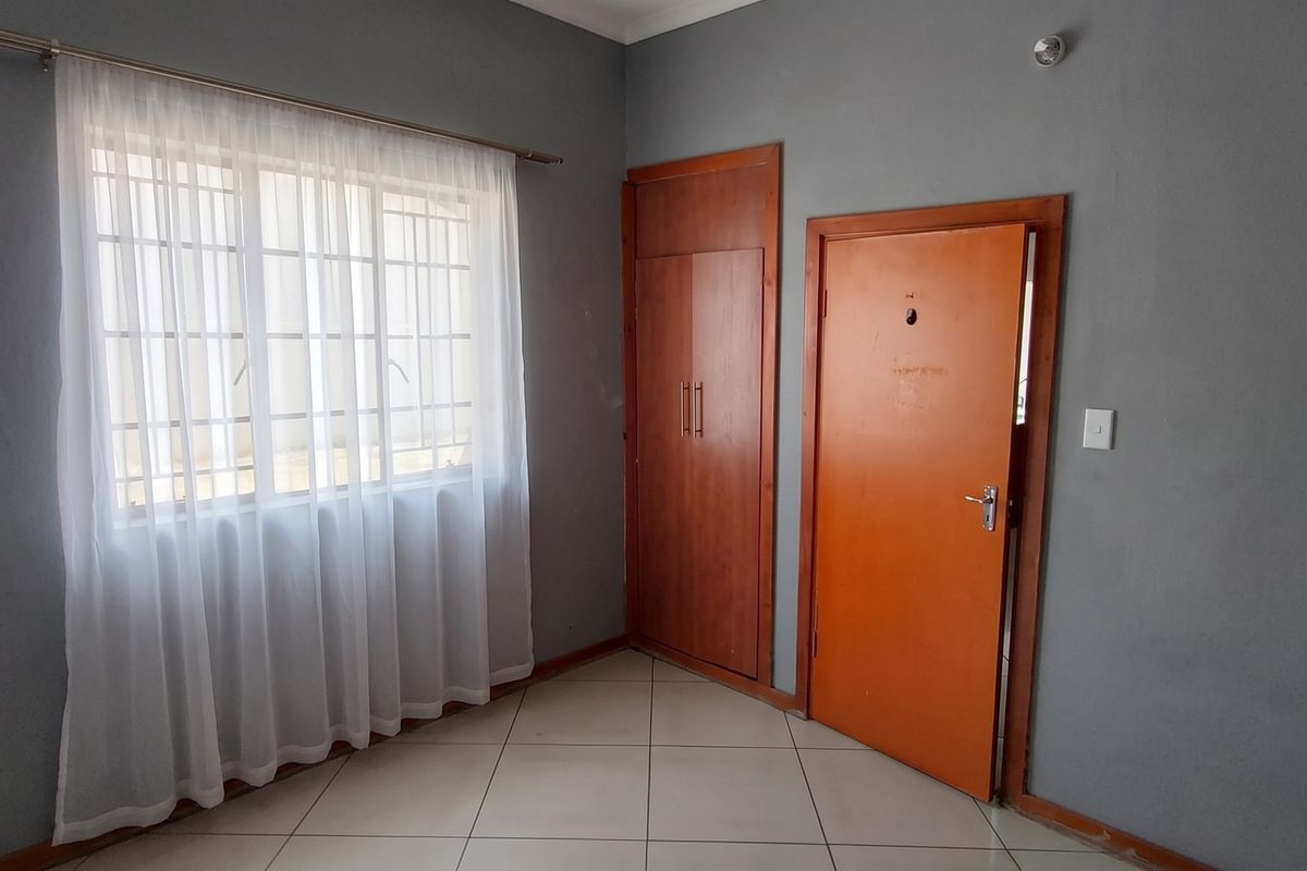 A vacant bedroom featuring tiled flooring, a built-in wardrobe, and a window with security bars, offering a neutral canvas for personalization.