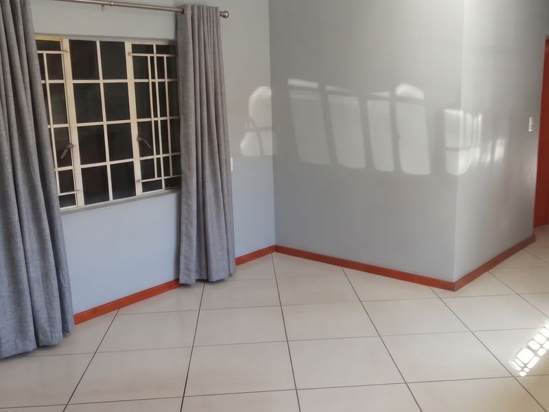 A bright, empty living area featuring neutral wall paint, tiled flooring, and a window fitted with security bars.
