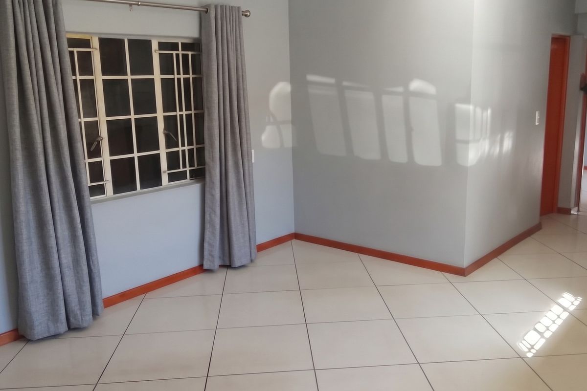 A bright, empty living area featuring neutral wall paint, tiled flooring, and a window fitted with security bars.