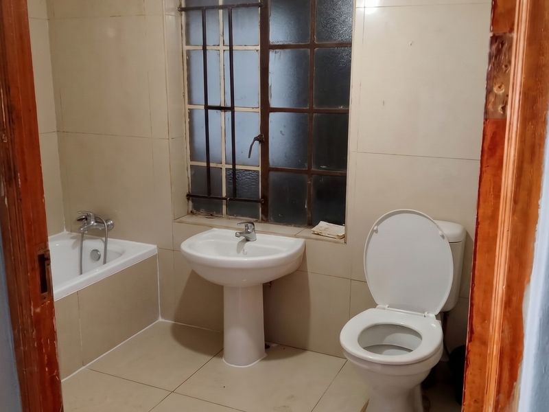 A functional bathroom featuring a pedestal basin, toilet, and bathtub with tiled finishes, requiring cosmetic updates to modernize the space.