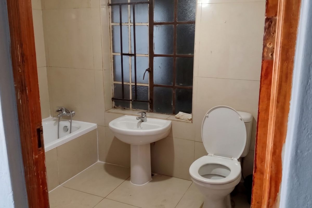 A functional bathroom featuring a pedestal basin, toilet, and bathtub with tiled finishes, requiring cosmetic updates to modernize the space.