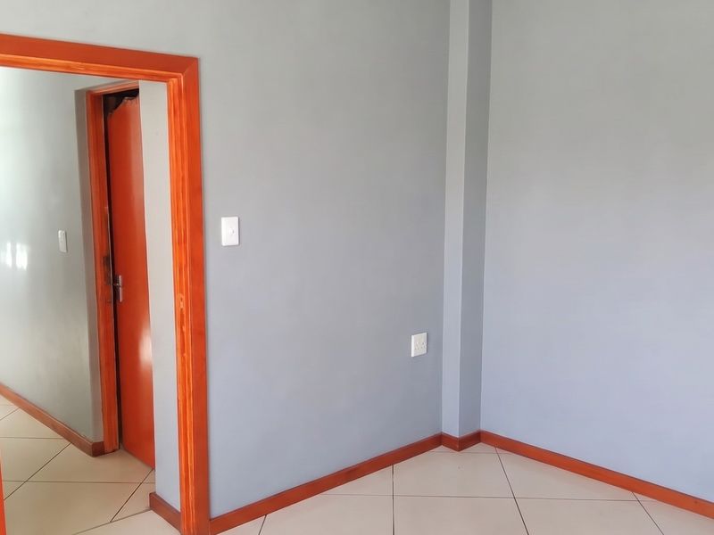 An empty bedroom featuring neutral grey walls, tiled flooring, and contrasting wooden door frames and skirting boards.