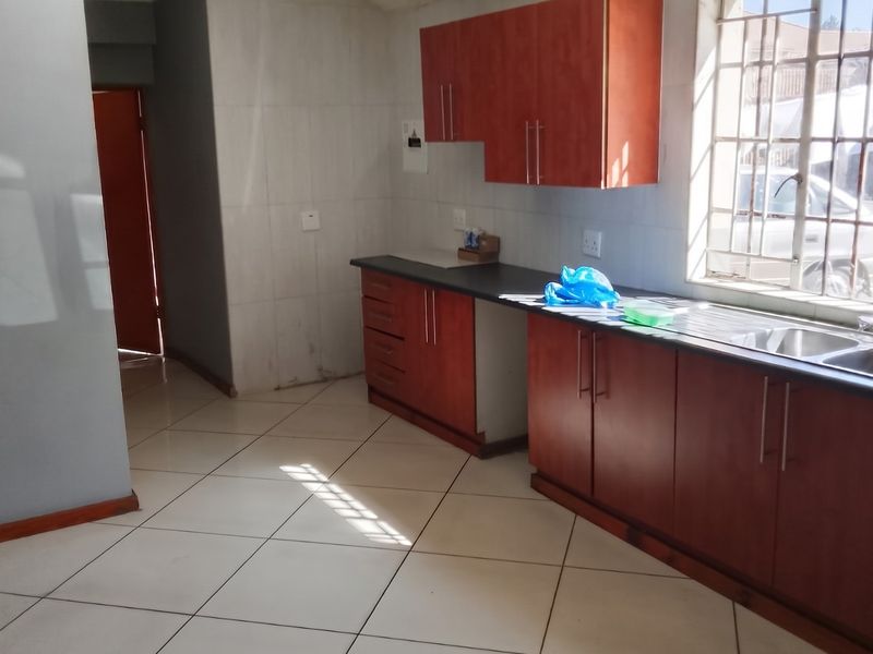 A functional kitchen featuring wooden cabinetry, laminate countertops, a double stainless steel sink, and tiled flooring with natural light from a window.