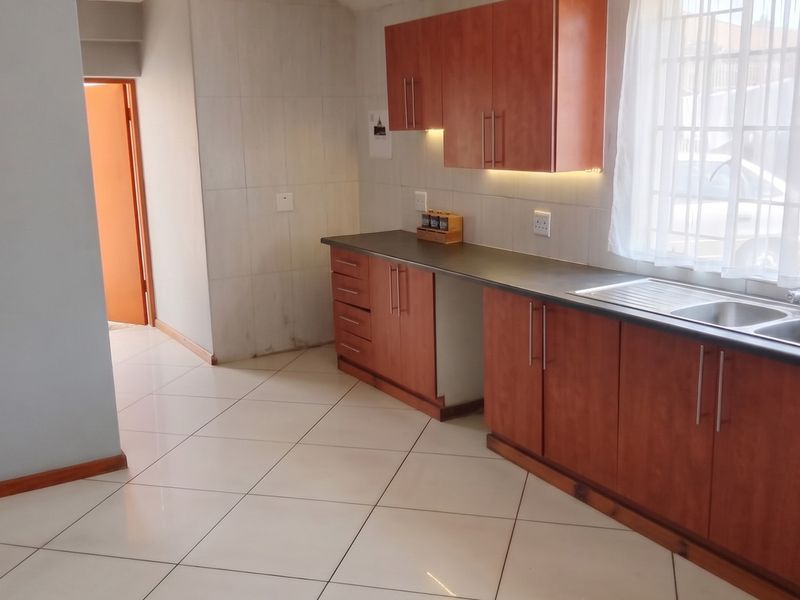A functional kitchen featuring wood-look laminate cabinetry, dark countertops, a double stainless steel sink, and neutral ceramic floor tiles.