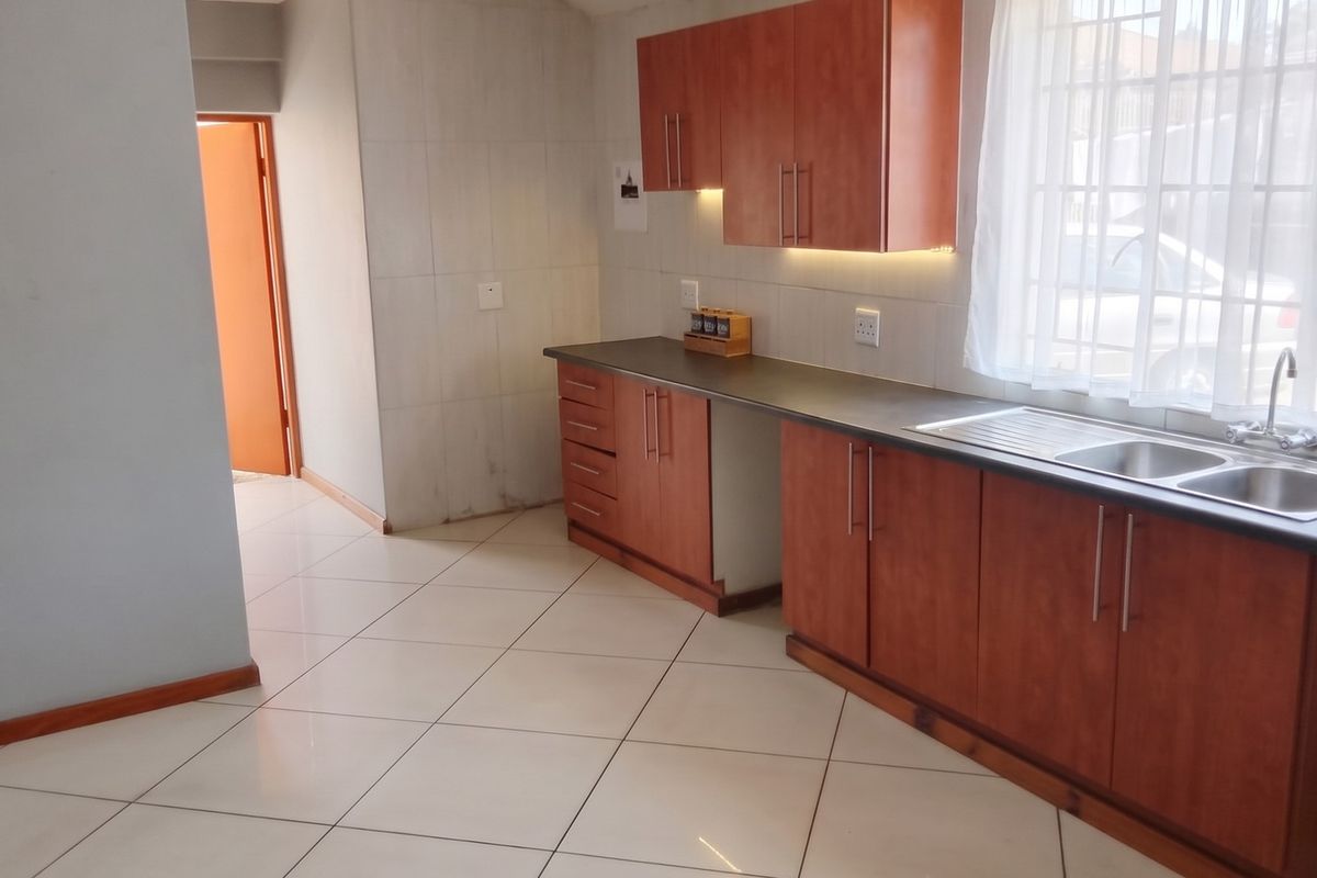A functional kitchen featuring wood-look laminate cabinetry, dark countertops, a double stainless steel sink, and neutral ceramic floor tiles.