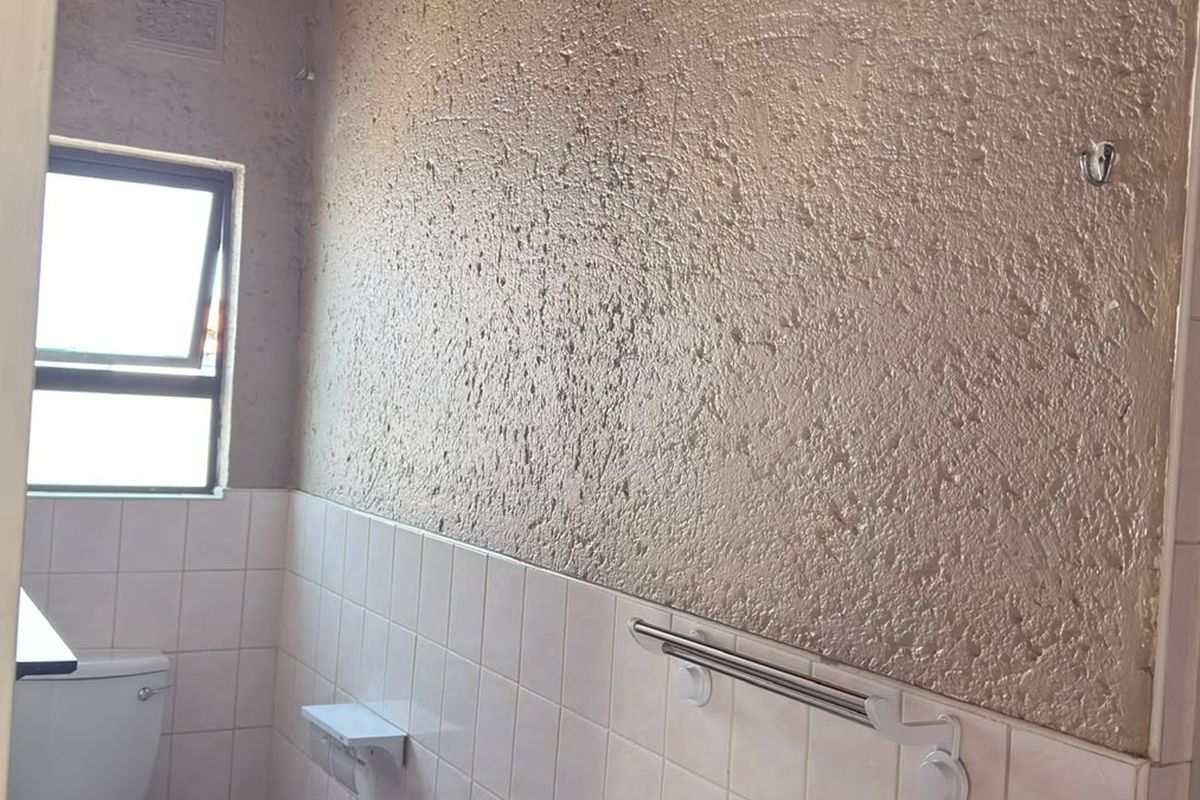 A functional bathroom featuring a toilet, tiled lower walls, and a textured upper wall finish, offering potential for a modern renovation.