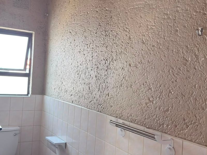 A functional bathroom featuring a toilet, tiled lower walls, and a textured upper wall finish, offering potential for a modern renovation.