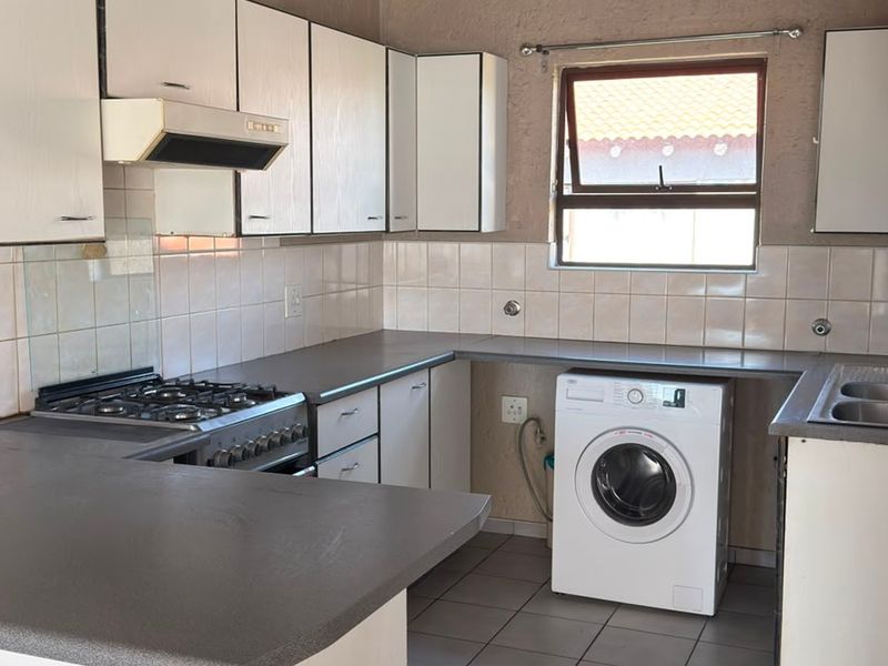 A functional kitchen featuring built-in cabinetry, a gas hob with extractor, tiled backsplash, and a stainless steel sink with space for a washing machine.