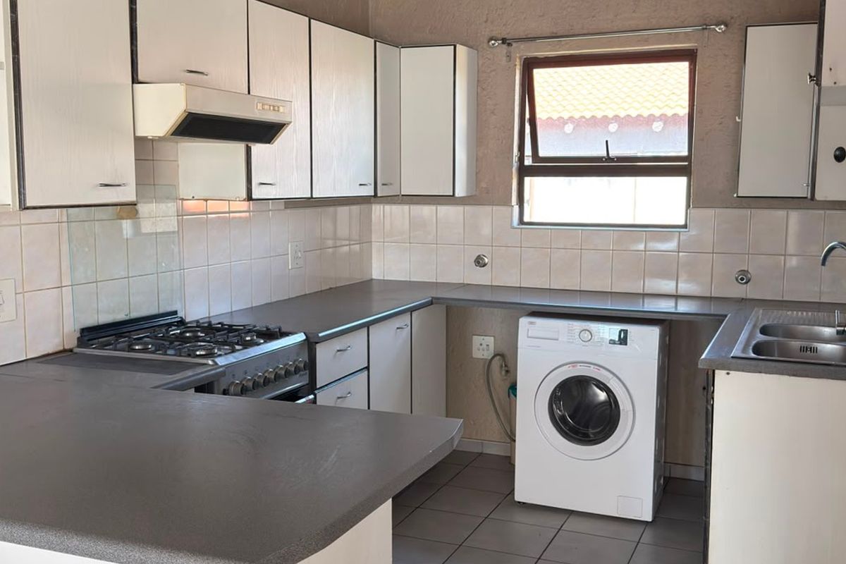 A functional kitchen featuring built-in cabinetry, a gas hob with extractor, tiled backsplash, and a stainless steel sink with space for a washing machine.