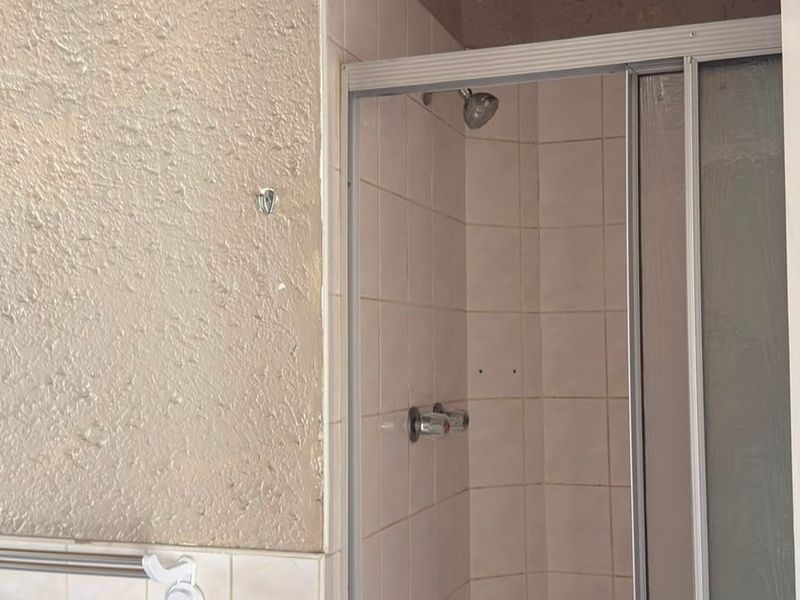 A dated bathroom featuring a shower enclosure with tiled walls and a standard shower mixer, requiring cosmetic updates to modernize the space.