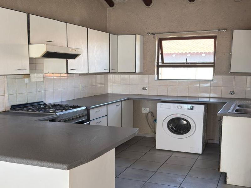 Functional kitchen featuring white cabinetry, gas hob with extractor, tiled backsplash, and dedicated space for a washing machine under the countertop.