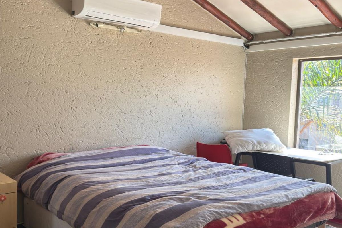 A bedroom featuring textured walls, exposed timber ceiling beams, and a wall-mounted air conditioning unit.