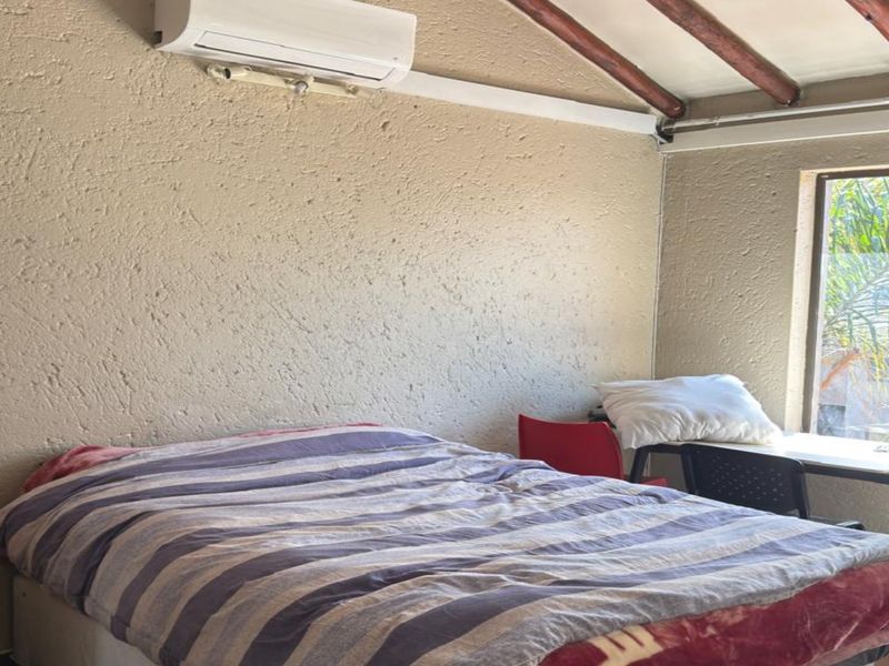 A bedroom featuring textured walls, exposed timber ceiling beams, and a wall-mounted air conditioning unit.