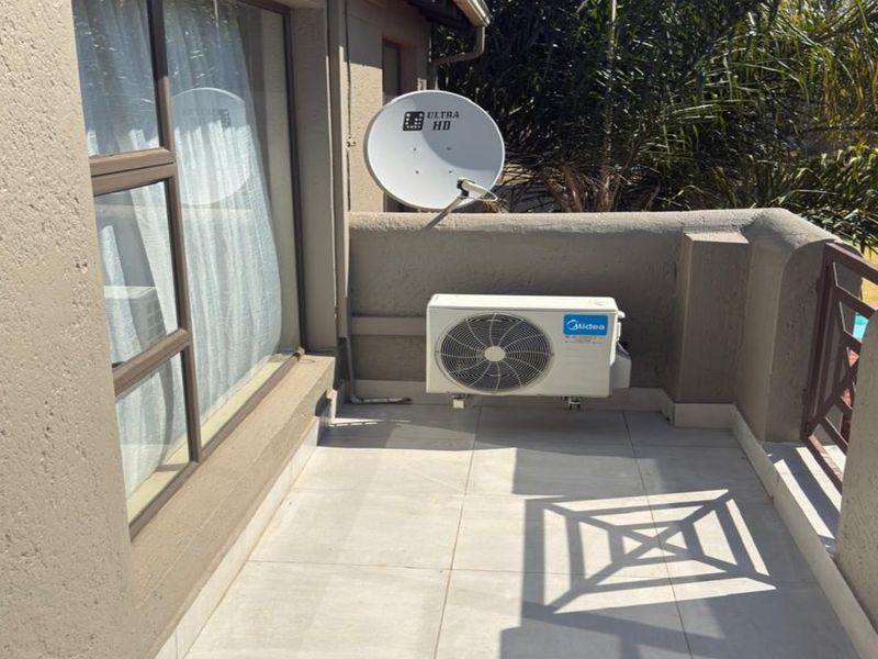 A private balcony featuring tiled flooring, a mounted air conditioning condenser unit, and a satellite dish, overlooking the surrounding garden area.