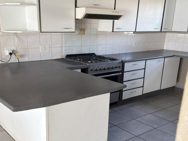 A functional kitchen featuring white cabinetry, dark laminate countertops, a gas stove with extractor fan, and tiled flooring, offering a clean, blank canvas for updates.